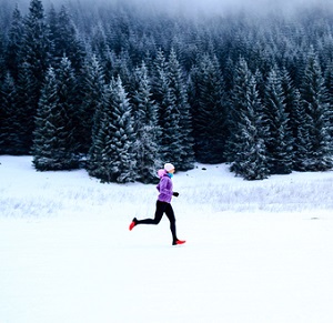 Kvinna som springer i skogen på vintern
